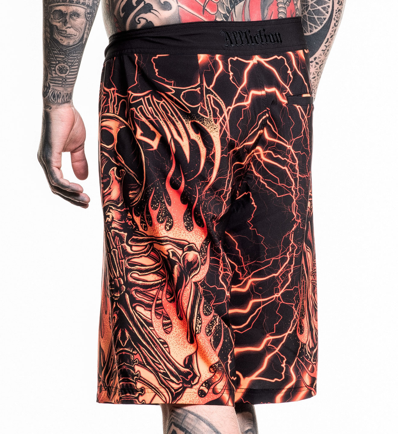 Infernal Nightmare Boardshort featuring fiery skeleton and lightning design with 4-way stretch fabric in size 32 worn by tattooed model.